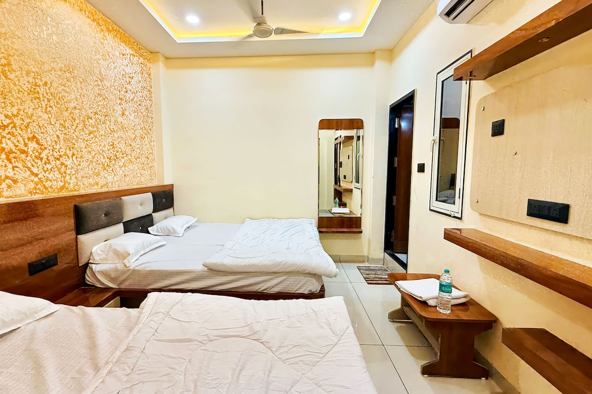 A hotel room with two beds, a bedside table with a bottle, a mirror, and a ceiling fan.