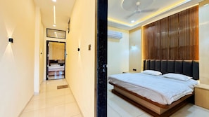 A hotel room with a bed, a ceiling fan, and a wall-mounted air conditioning unit. - Hotel Rishant Palace (Omkareshwar)