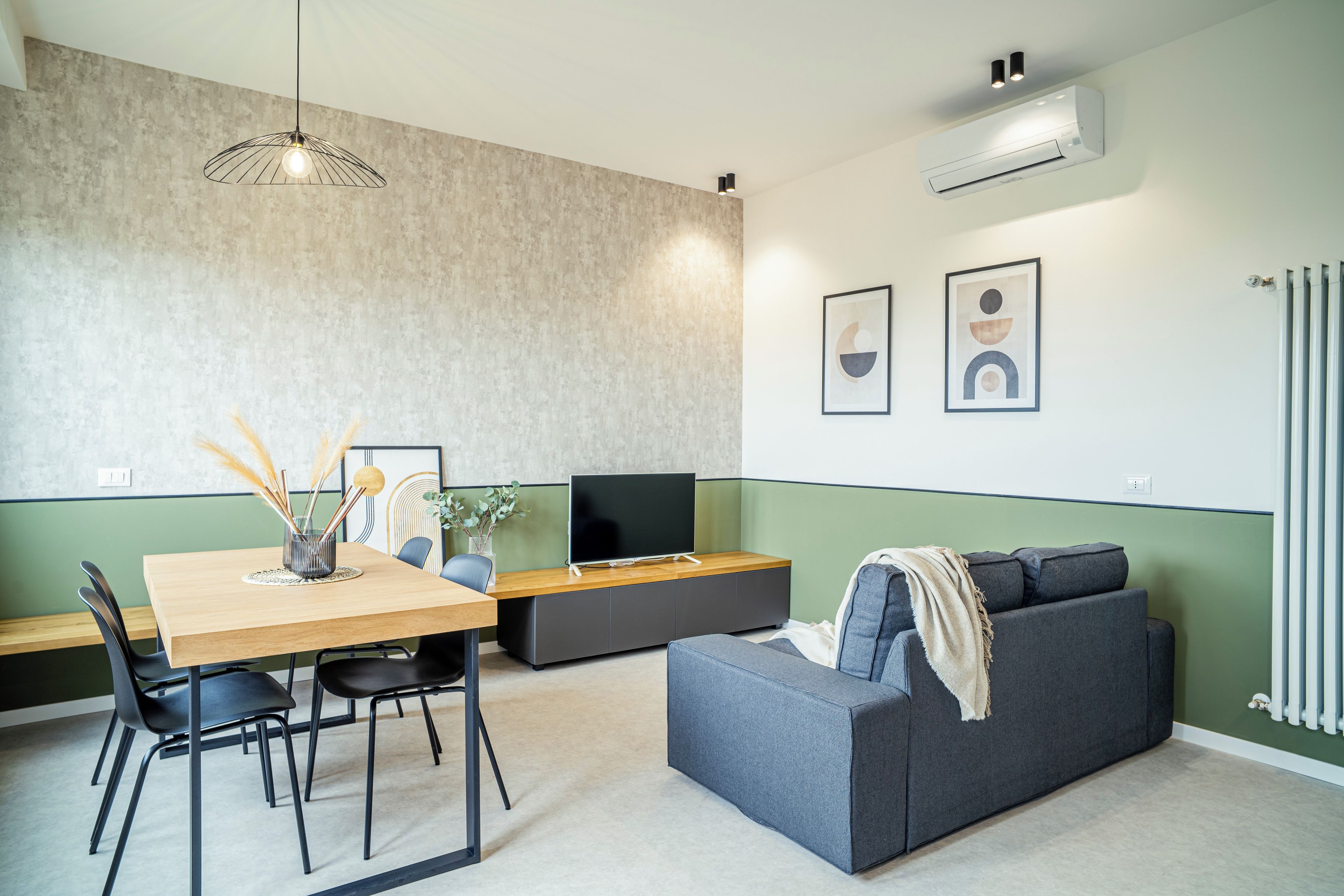 Una sala moderna con comedor, un sofá gris, un televisor de pantalla plana y un aire acondicionado instalado en la pared.