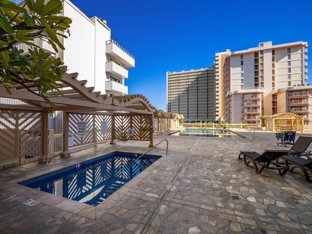 Zona de piscina con piscina, sillas de descanso y vistas de edificios circundantes.