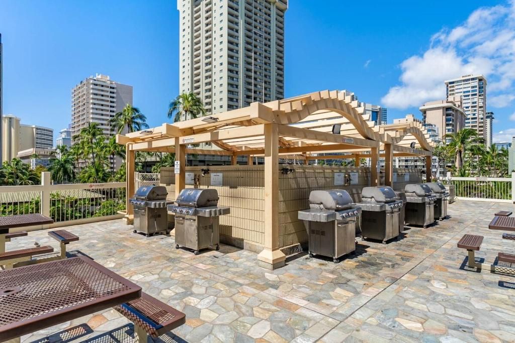 Un patio exterior con varias parrillas, una pérgola de madera y suelo de piedra.