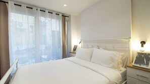 Une chambre d’hôtel comprenant un lit, une table de chevet, une commode, une fenêtre avec des rideaux et un luminaire fixé au mur.