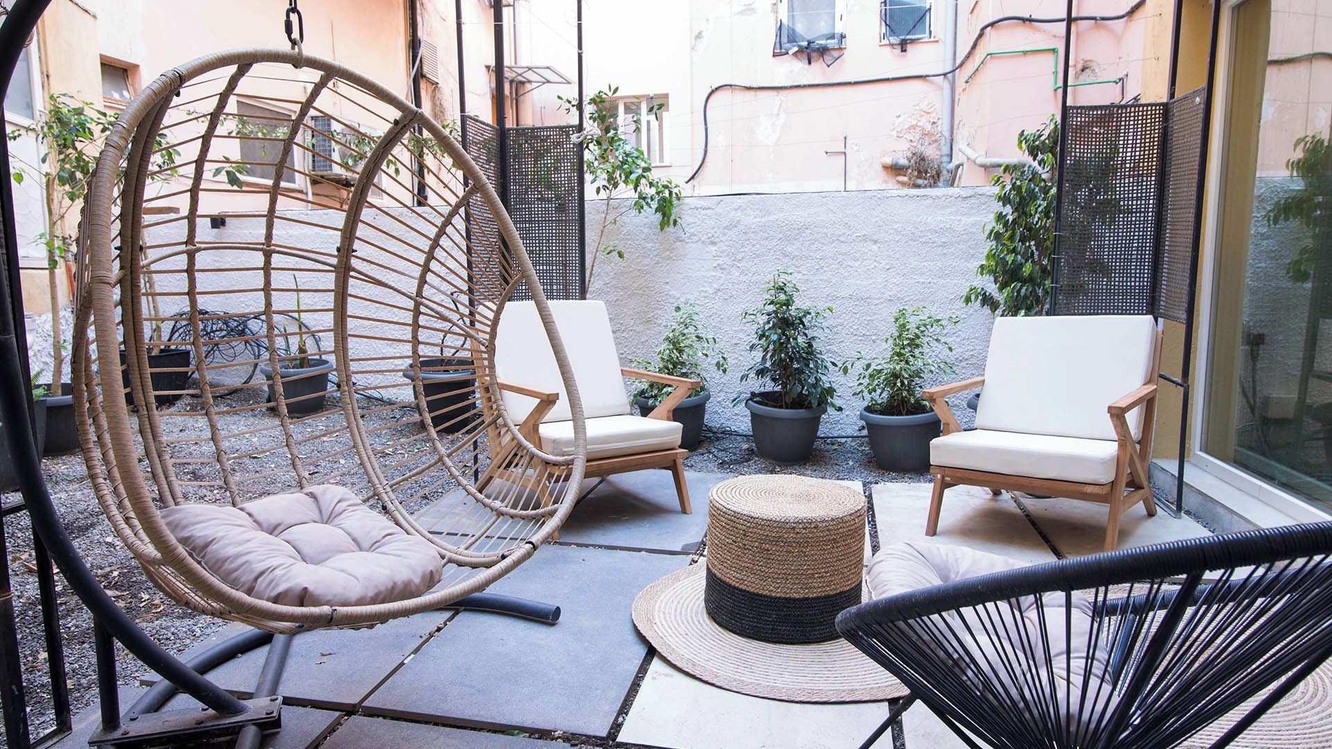 Een terras met twee rieten stoelen, een hangstoel en een rond geweven poef.