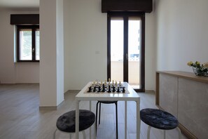 Una habitación con un tablero de ajedrez sobre una mesa, dos sillas, una ventana y una puerta.