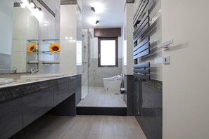 Un baño moderno con cabina de ducha de vidrio, inodoro y un espejo grande decorado con un girasol.