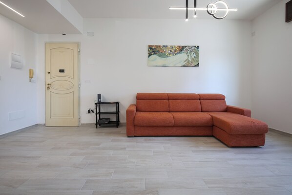 Una habitación con una puerta color beige, un sofá rojo, un cuadro en la pared y un estante negro.