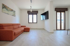 Un salón amplio con sofá, televisor de pantalla plana en la pared y un ventanal grande.