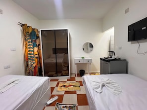Ein Hotelzimmer mit zwei Betten, einem kleinen Schreibtisch, einem Spiegel, einem Fernseher und einem Kleiderschrank.