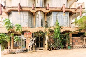 A building with a brick facade, large windows, and a statue of horses in front. - Meliva Guest House Mbarara (Mbarara)