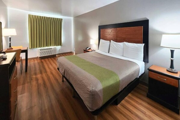 A hotel room with a bed, bedside tables, a desk, a lamp, a window with curtains, and a radiator.