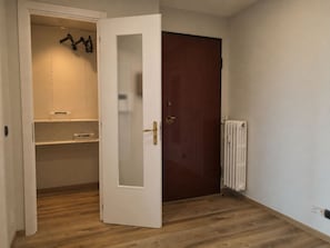 Une pièce avec un plancher en bois, une porte blanche dotée d’un panneau en verre dépoli, un radiateur et une armoire avec des étagères.
