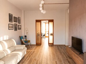 Un salon moderne avec un canapé, un téléviseur et un coin repas visible à travers une porte ouverte.