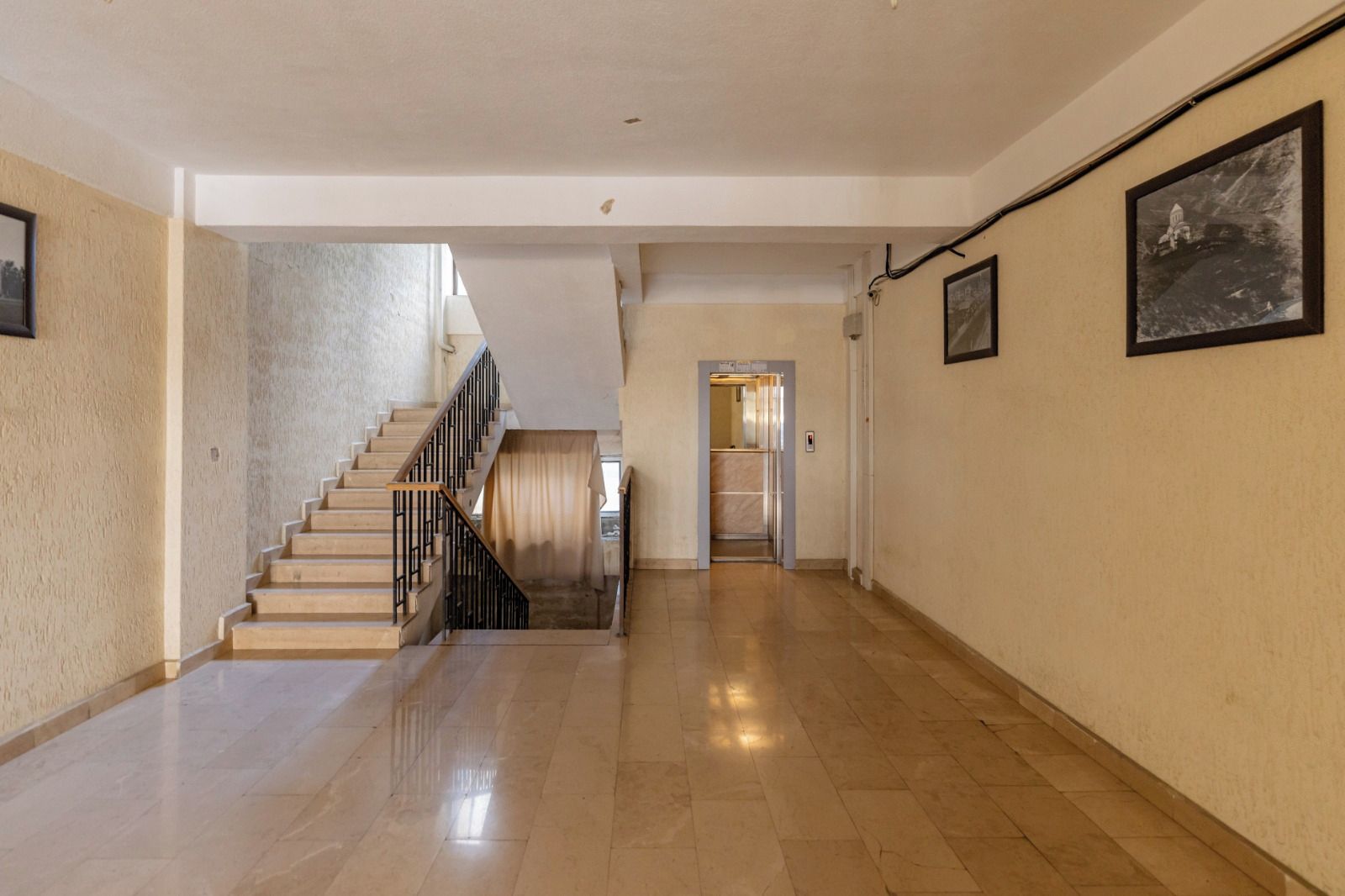 A hallway with a staircase, a door leading to an elevator, and a wall-mounted picture.