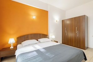 A hotel room with a large bed, two bedside tables with lamps, an orange accent wall, and a wooden wardrobe. - Prime Comfort Residence (Tbilisi)