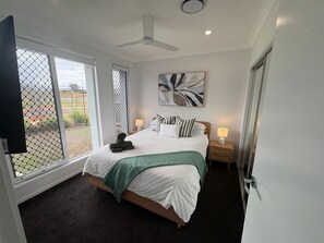 A bedroom with a bed, a ceiling fan, a window with a view, and a bedside table with a lamp. - Amaranthine Haven- 4 bed 2 bath entire house (Mango Hill)