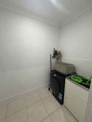 A laundry room with a washing machine, a basket, and a green basin. - Amaranthine Haven- 4 bed 2 bath entire house (Mango Hill)