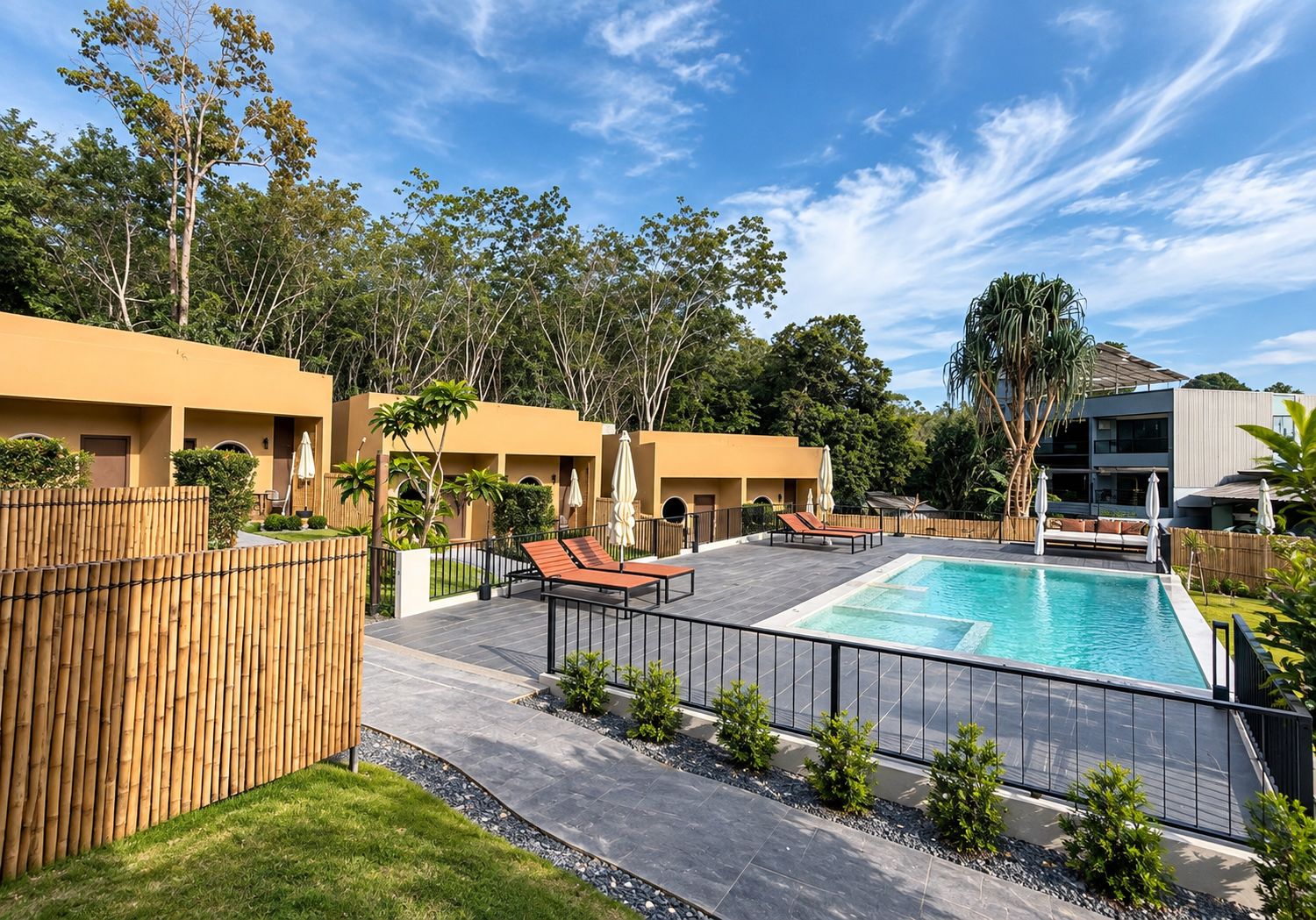 A pool area with lounge chairs and a swimming pool, surrounded by a bamboo fence and greenery.