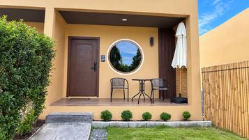 A modern building with a brown door, a round window, and a small patio with two chairs and a table.