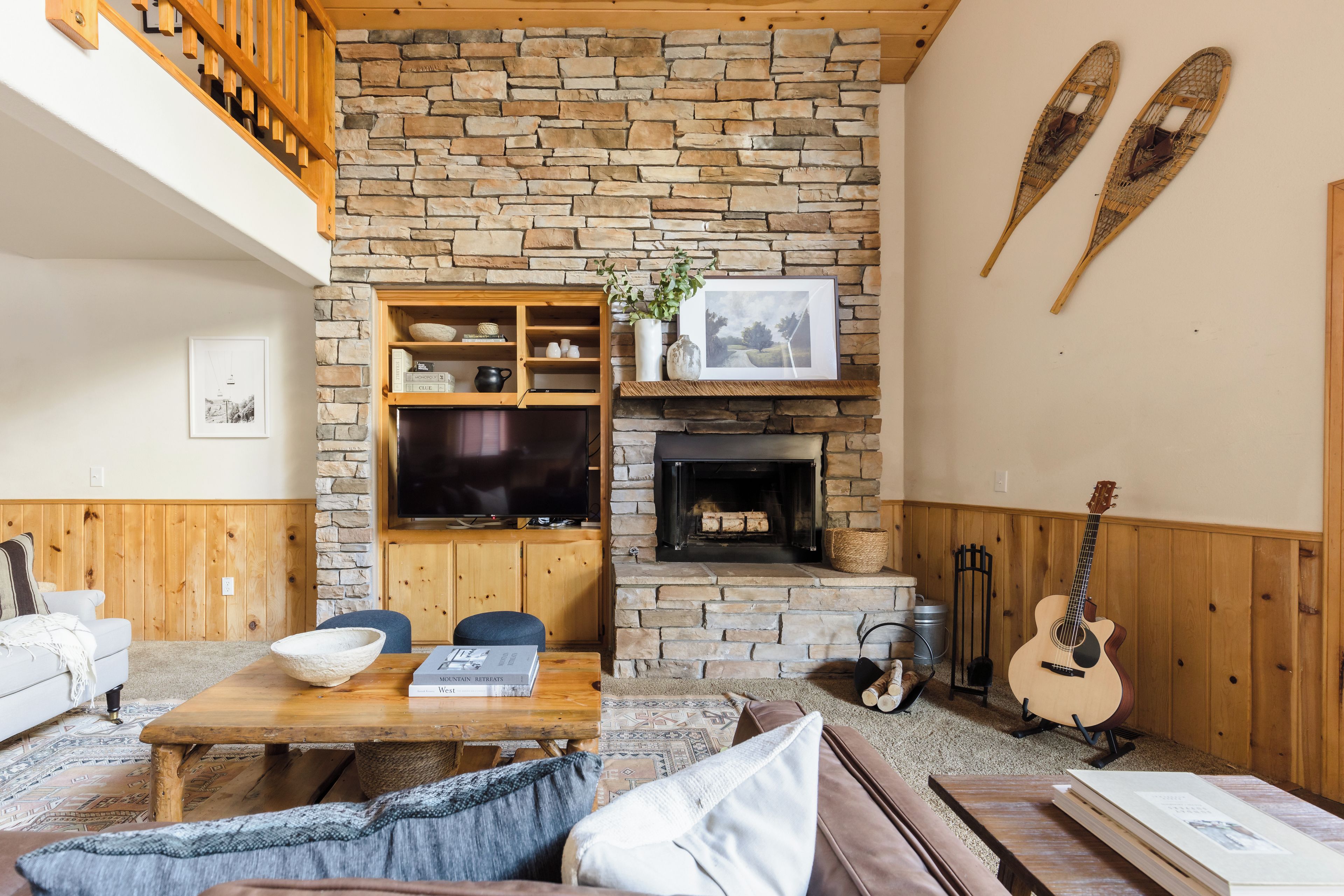 Una sala de estar acogedora con chimenea de piedra, muebles de madera y un televisor montado.