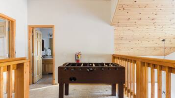 A room with a wooden foosball table, a wooden railing, and a door leading to a bathroom.