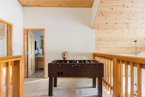 Habitación con mesa de futbolín de madera, barandilla de madera y puerta que da a un baño.