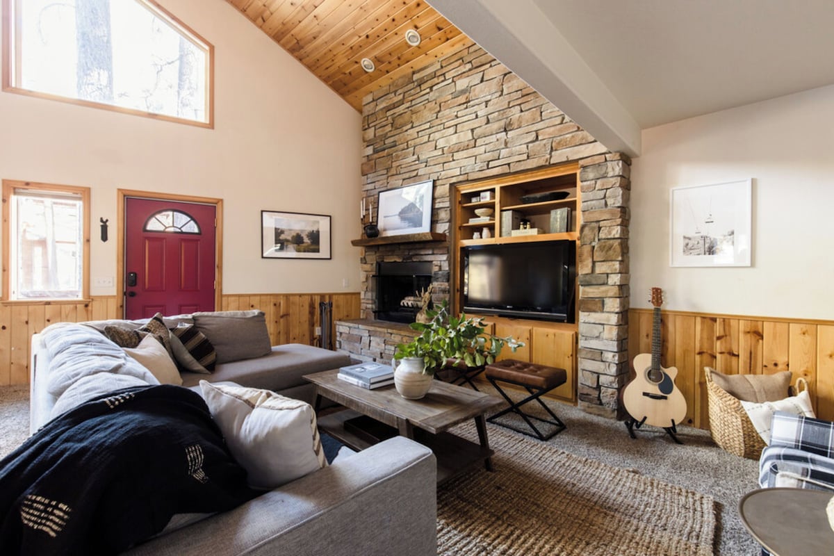 Ein gemütliches Wohnzimmer mit Kamin aus Stein, einem Fernseher und einer Gitarre.