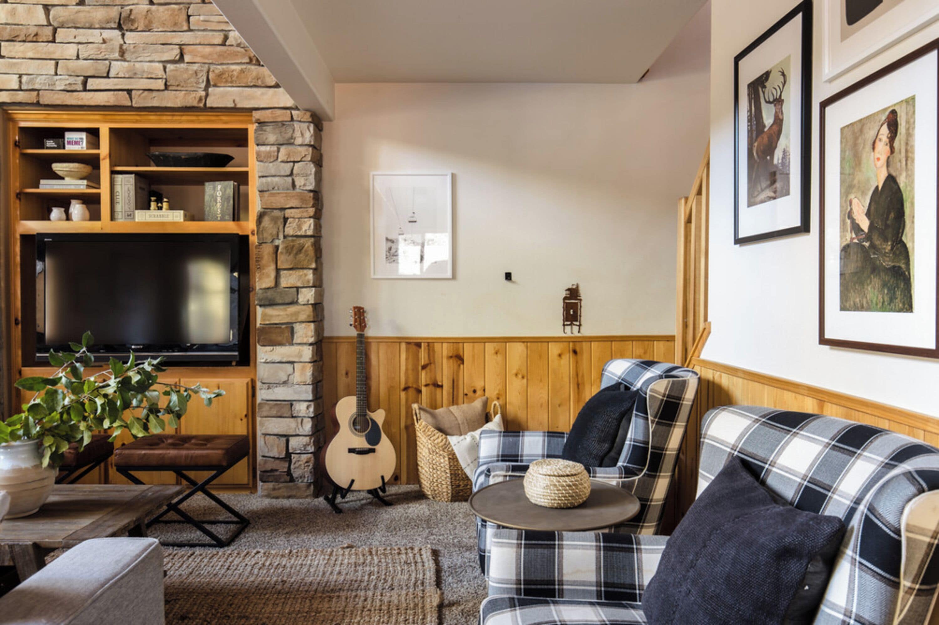 A cozy living room with a stone wall, a television, a guitar, a sofa, and a coffee table.