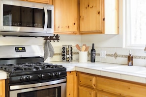 Una cocina con microondas, estufa, armarios de madera y salpicadero de azulejos.
