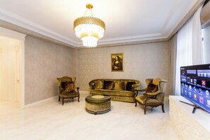 A living room with a chandelier, a sofa set, two armchairs, a round coffee table, and a flat-screen TV. - 2 Bedroom Deluxe Apartment In The City Center (Tbilisi)