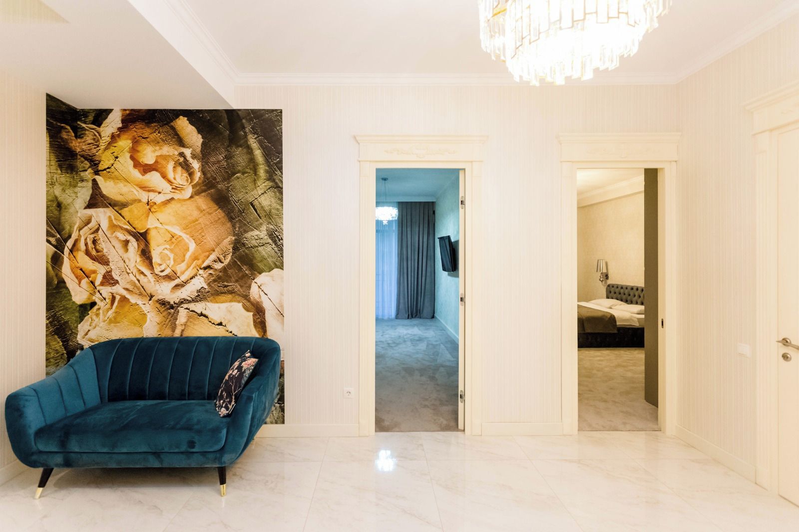 Ein Zimmer mit einem blauen Sofa, einem großen Blumenwandbild und einer Chandelier.