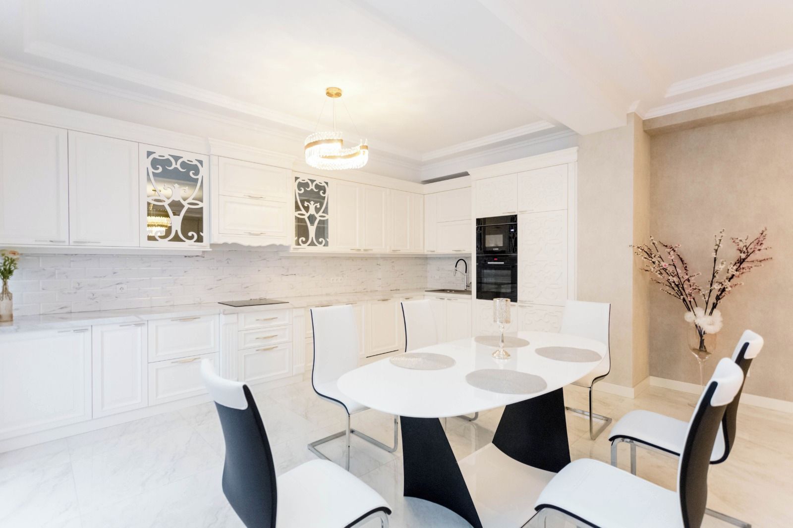 A modern kitchen with white cabinetry, a marble countertop, and a dining area with a round table and chairs.