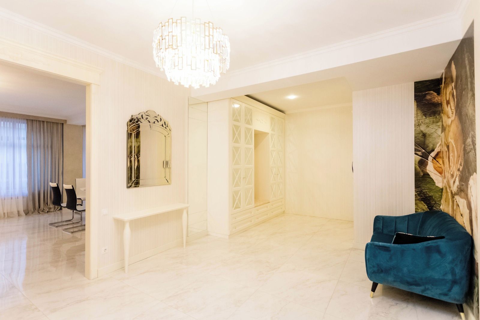 A spacious living room with a chandelier, a blue sofa, and a large mirror.