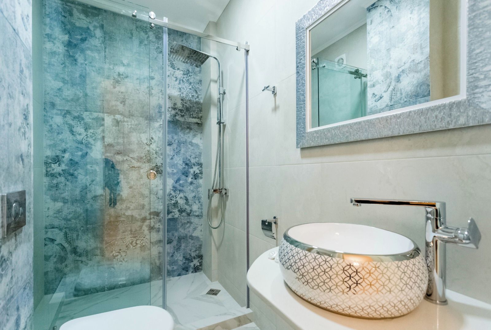 A bathroom with a glass-enclosed shower, a white sink with a patterned basin, and a mirror above the sink.