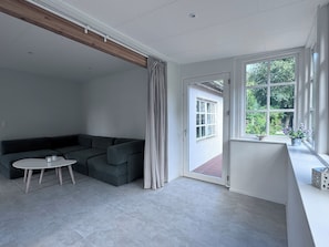 Una sala moderna con un sofá seccional gris, una mesita redonda y un ventanal corredero que da a un espacio exterior.