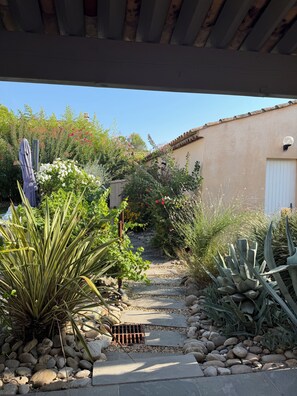 Un chemin de jardin qui mène à un bâtiment à la façade beige et à la porte blanche.