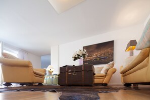 Un salon avec deux fauteuils en cuir, une valise ancienne et un tableau représentant un paysage urbain accroché au mur.