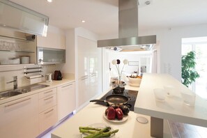 Une cuisine moderne dotée d’un îlot central, d’appareils électroménagers en acier inoxydable et d’un pare-feu en verre.