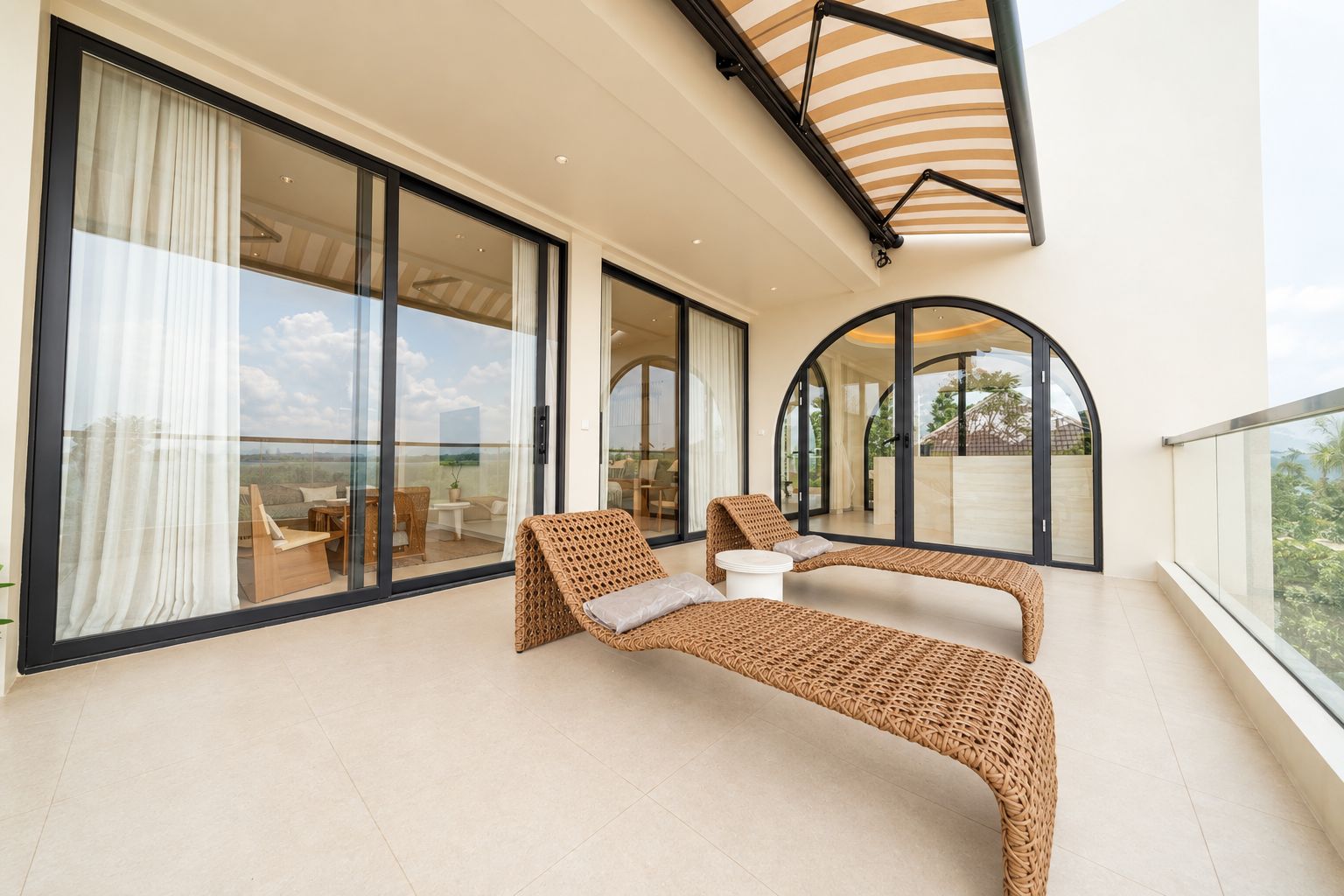 Ein Balkon mit Korbsessel, kleinem Tisch und Glastür zu einem Sitzbereich im Freien.