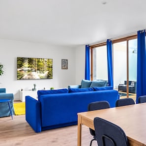 Un salon moderne avec un canapé bleu, une table à manger et une grande fenêtre avec des rideaux.