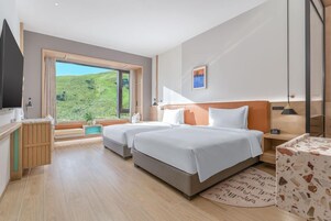 Habitación de hotel moderna con dos camas, un ventanal grande y vistas a zonas verdes.