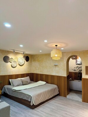 A bedroom with a bed, wooden headboard, wall-mounted lights, and a bathroom visible through an archway. - LushStay X Phan Đình House  (Ba Dinh)