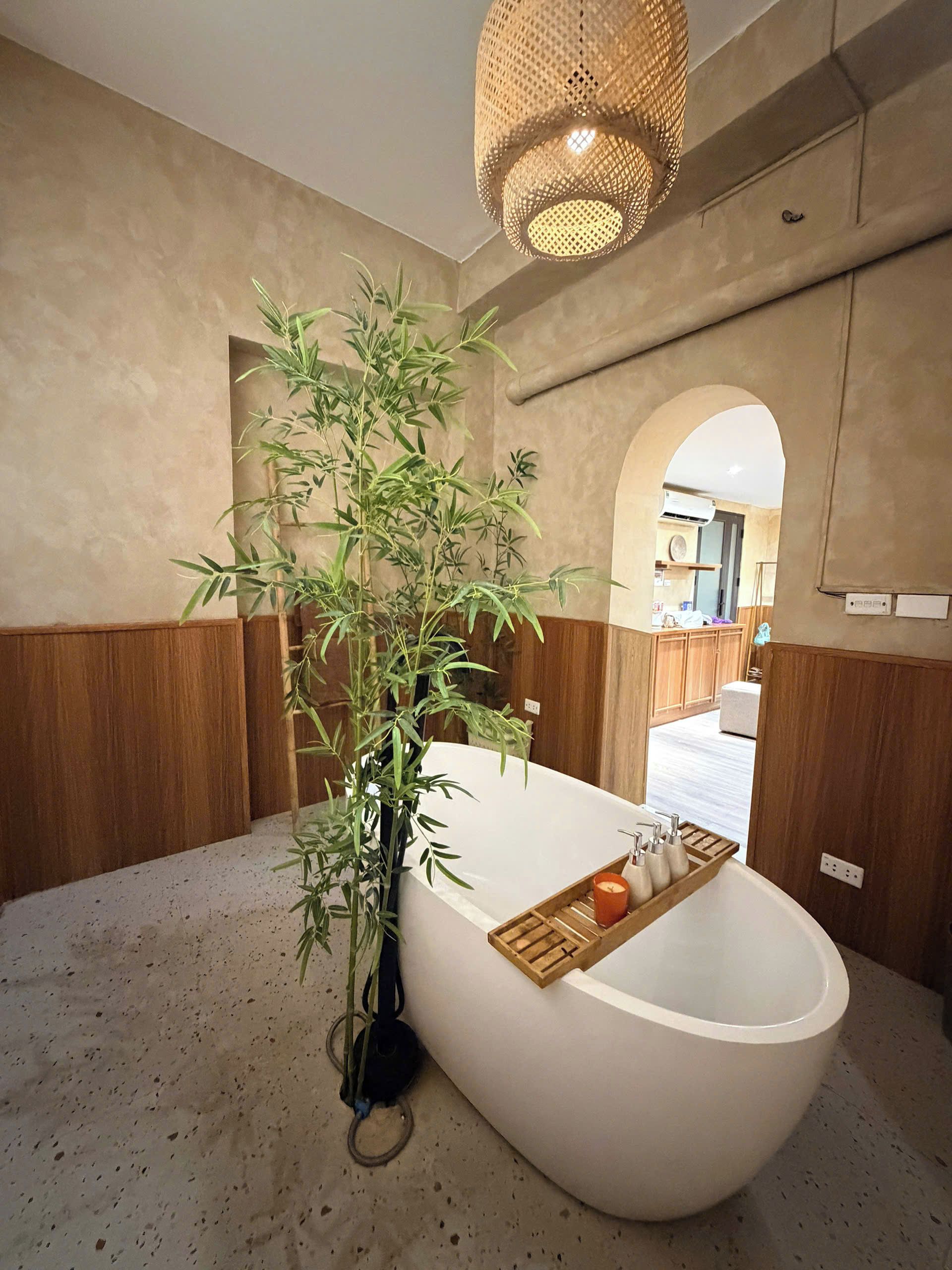 A modern bathroom with a freestanding bathtub, a bamboo plant, and a woven light fixture.