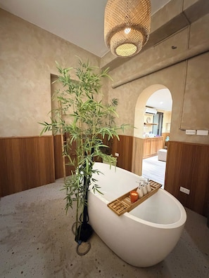 A modern bathroom with a freestanding bathtub, a bamboo plant, and a woven light fixture. - LushStay X Phan Đình House  (Ba Dinh)