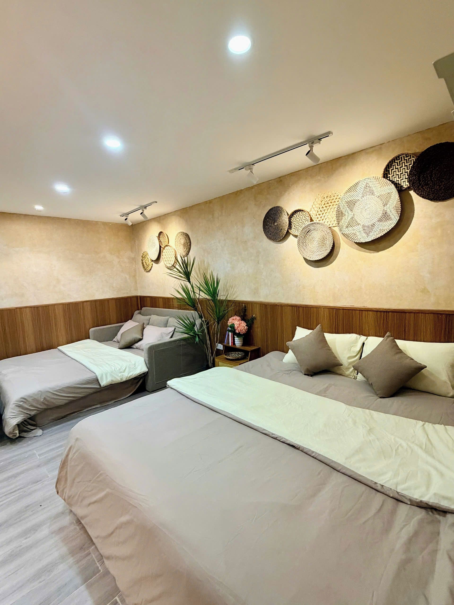 A hotel room with two beds, a wooden headboard, a wall-mounted light fixture, and a small table with a vase of flowers.