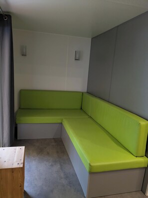 Una habitació amb una panca tapissada de verd, una taula de fusta i una paret amb relleny gris.