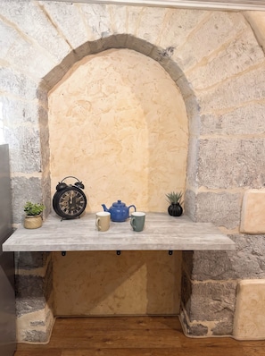 A stone archway with a shelf holding a clock, a teapot, and two cups. - New Listing (cahors)