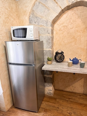A stainless steel refrigerator with a microwave on top, a small potted plant, a vintage alarm clock, and a blue teapot on a shelf. - New Listing (cahors)