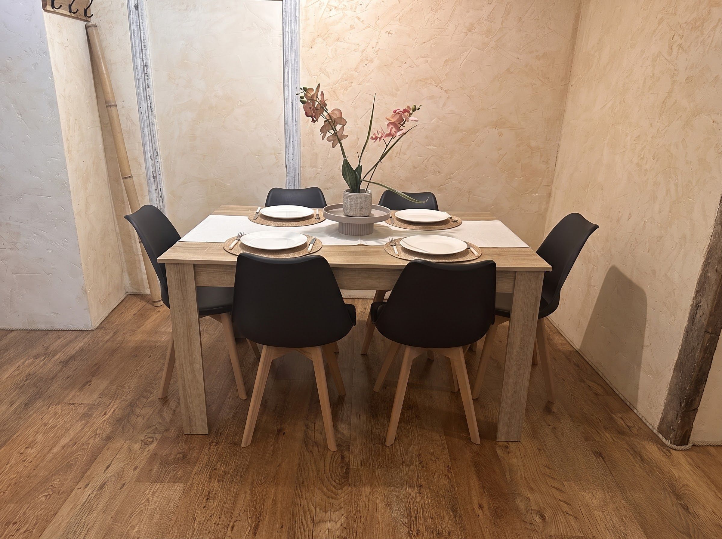 A dining table with six chairs, a vase with flowers, and a wooden floor.