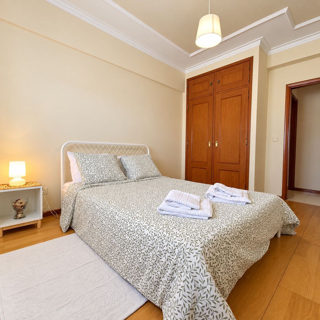 Un dormitorio con cama, mesita de noche, armario de madera y lámpara colgante.
