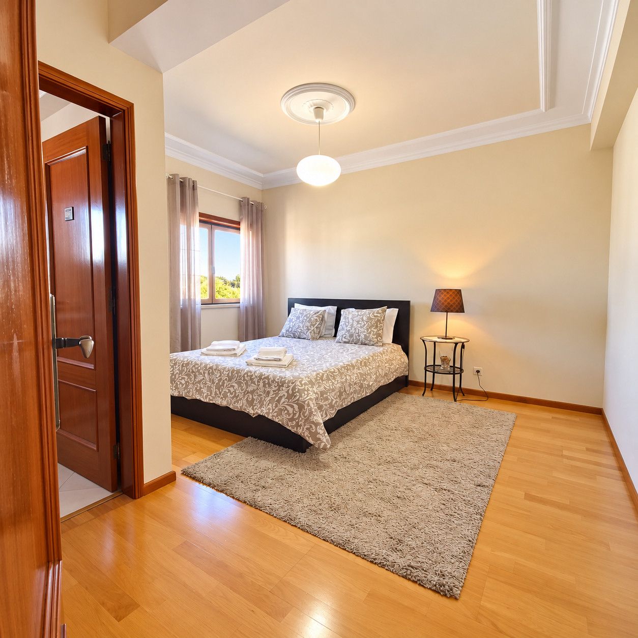 A bedroom with a bed, a bedside table with a lamp, a window with curtains, and a door.